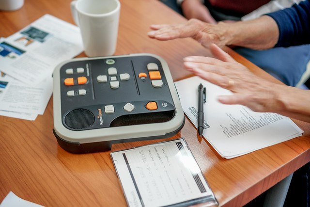 Table with meetings notes and audio reader and ladies hands reaching for the audio reader